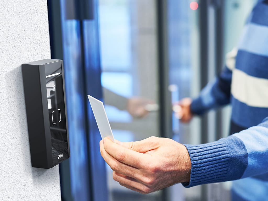 白い壁に取り付けられた高品質な黒い2N IPアクセス制御リーダーを介して、RFIDアクセスカードを使ってドアのロックを解除する人物。