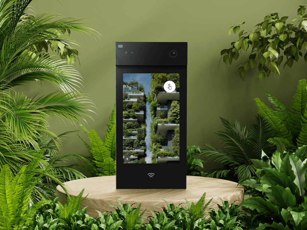 Black 2N intercom displayed on a wooden pedestal surrounded by lush green plants and a green wall.