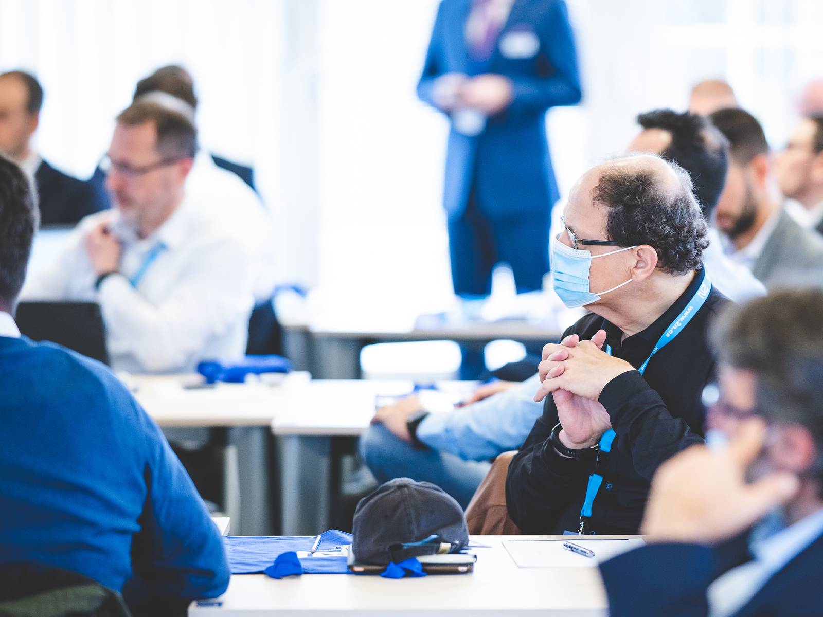 Deelnemers zitten in een heldere conferentieruimte en luisteren aandachtig tijdens een professionele vergadering of seminar.
