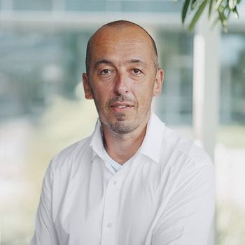 Person in a white shirt sitting indoors in a bright, modern office environment.