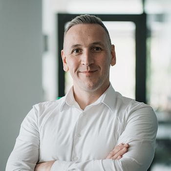 Person in a white shirt standing confidently with arms crossed in a modern office setting.