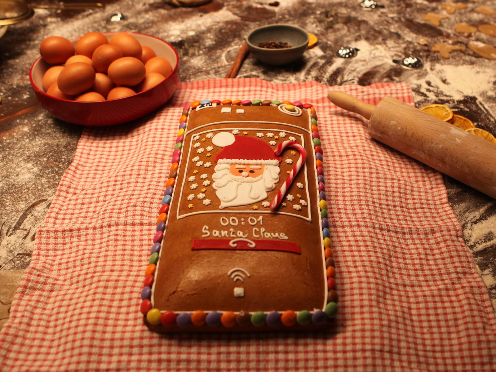 Pan di zenzero a forma di interfono 2N IP decorato con un design di Babbo Natale posizionato su un panno tra vari ingredienti e strumenti da forno.