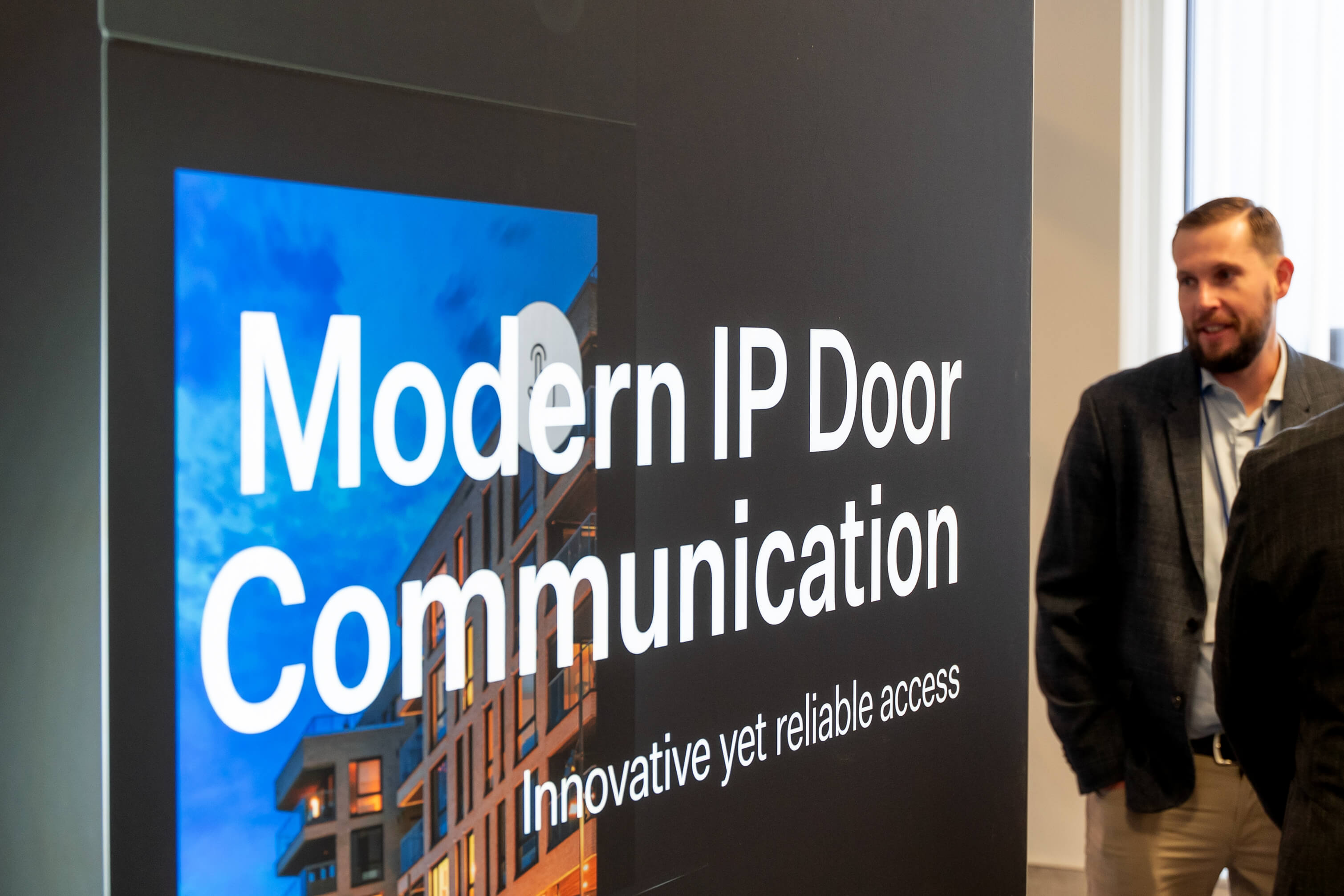 A man stands next to a large display reading "Modern IP Door Communication" at an exhibition.