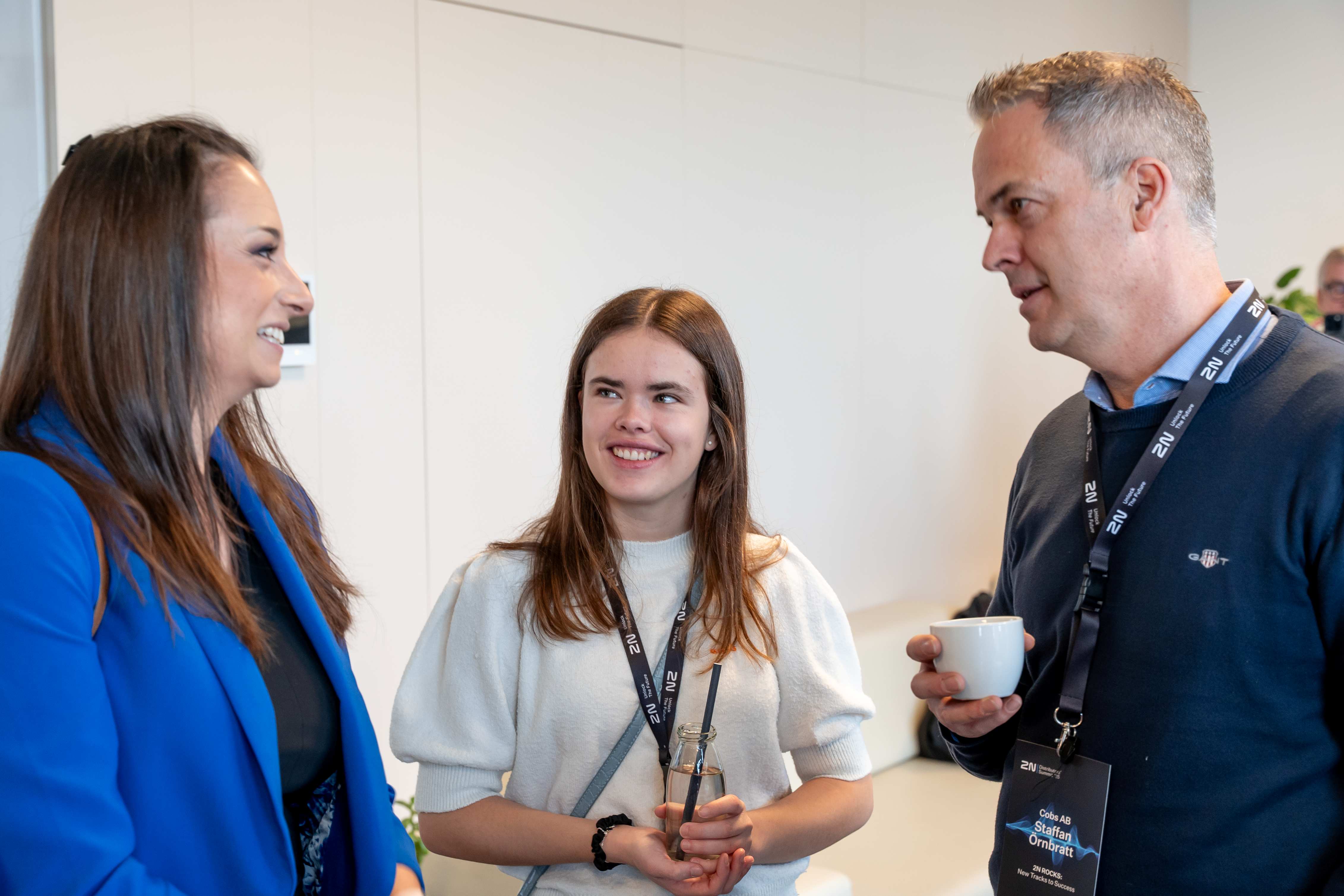 Three professionals engaging in a friendly conversation at a business event, holding coffee.