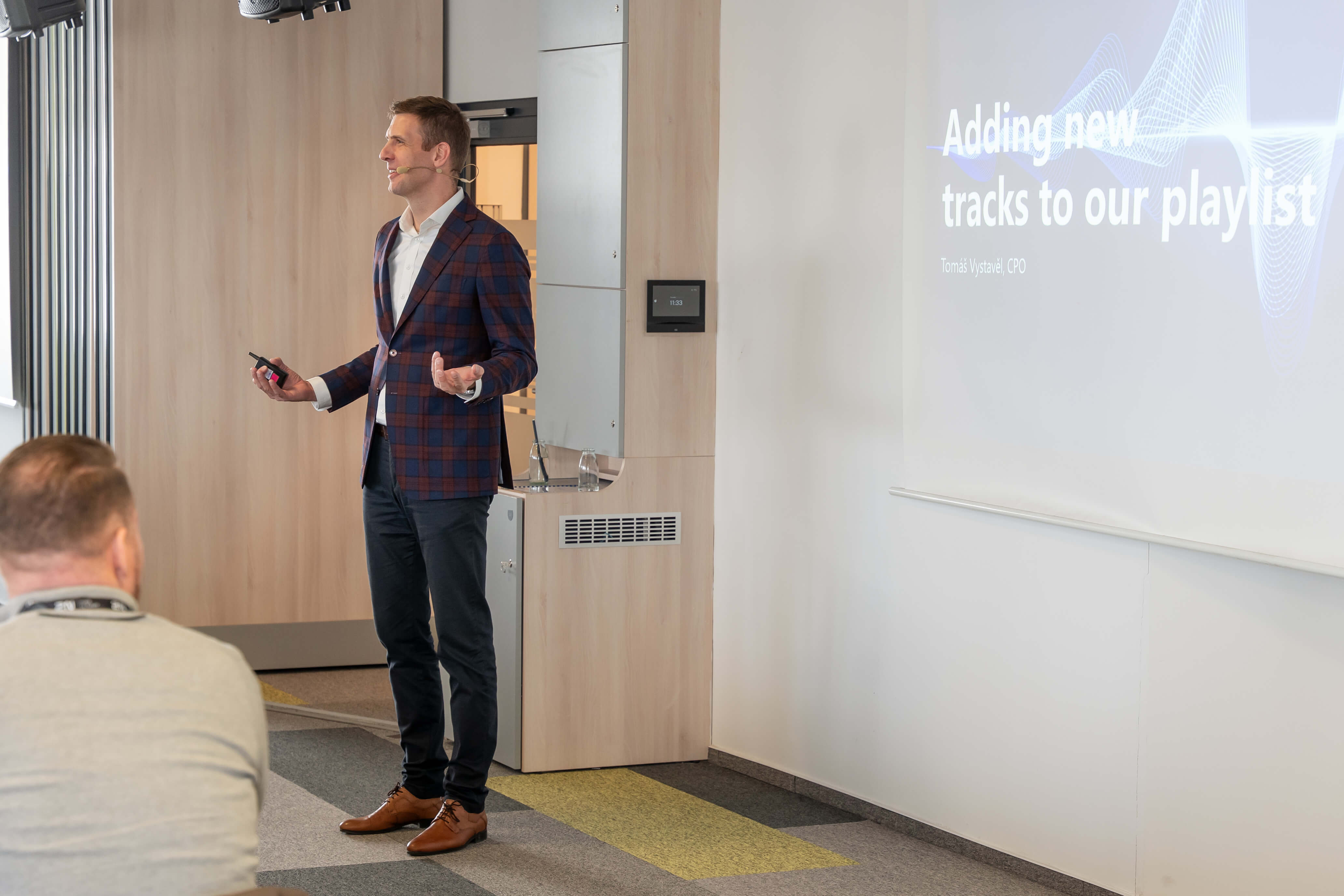 A presenter stands next to a screen displaying the title, "Adding new tracks to our playlist."