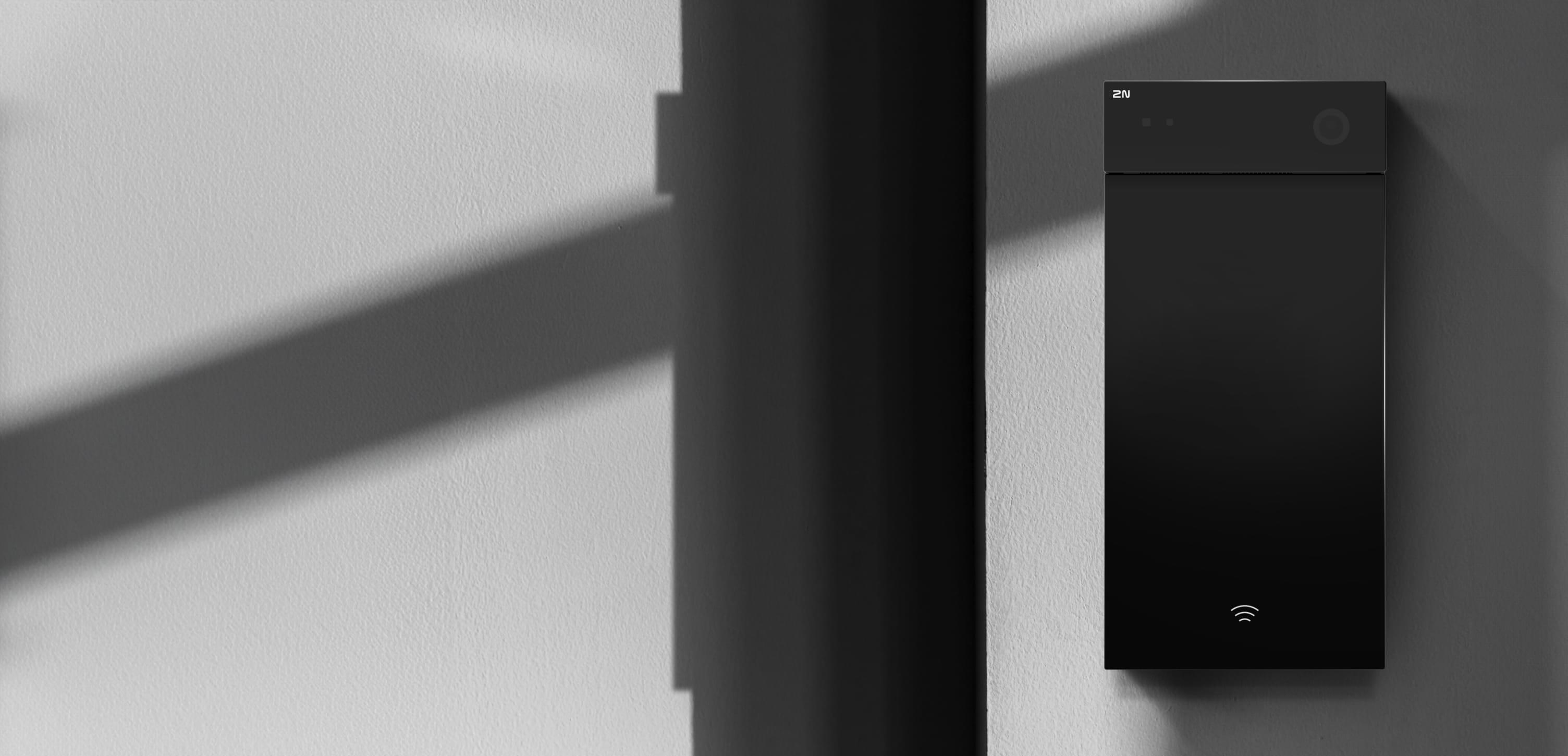 Image en noir et blanc d'un appareil intelligent moderne et élégant de forme rectangulaire noire monté sur un mur gris clair.