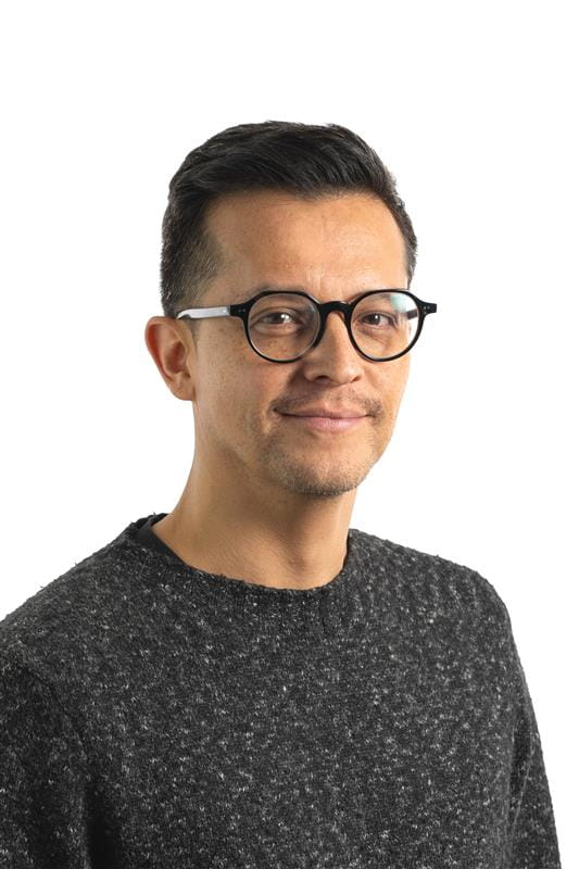 Photo du haut du corps d'un homme avec des lunettes, des cheveux noirs et un pull gris.