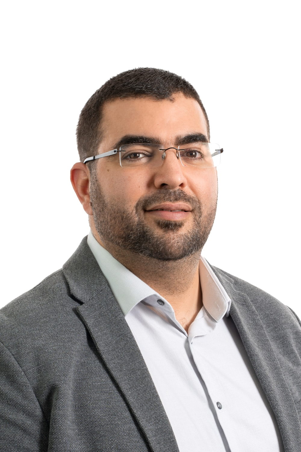Photo professionnelle d'un homme avec une barbe et des lunettes portant une chemise blanche et un blazer gris.