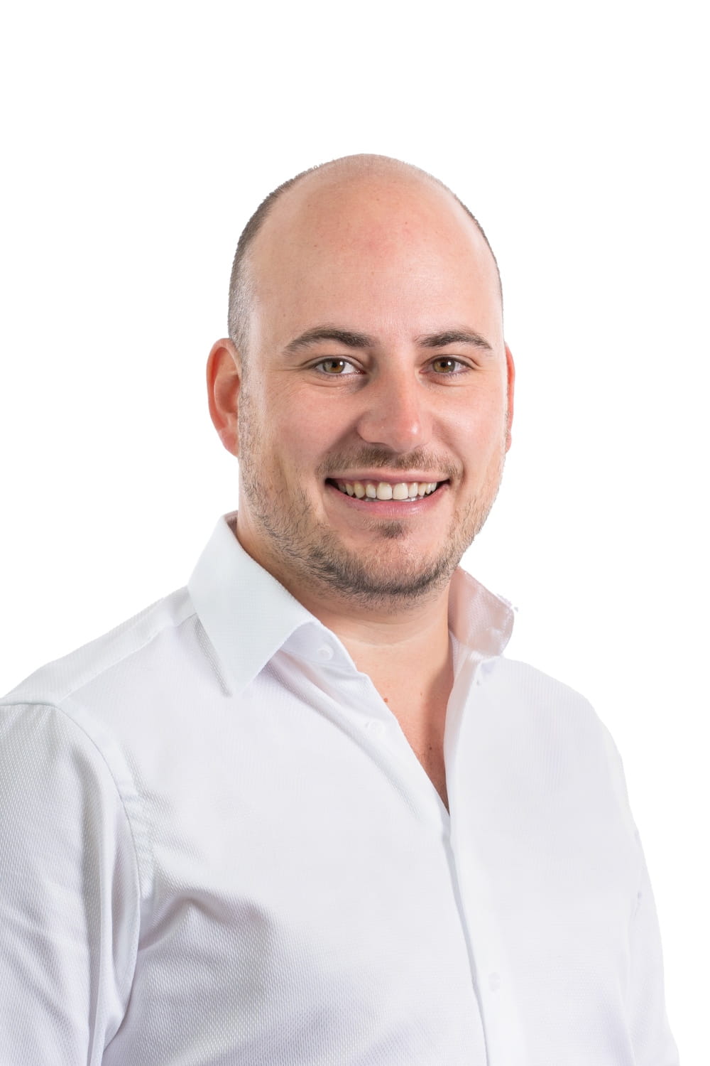 Photo professionnelle d'un homme souriant avec une tête rasée et une barbe, portant une chemise blanche impeccable.