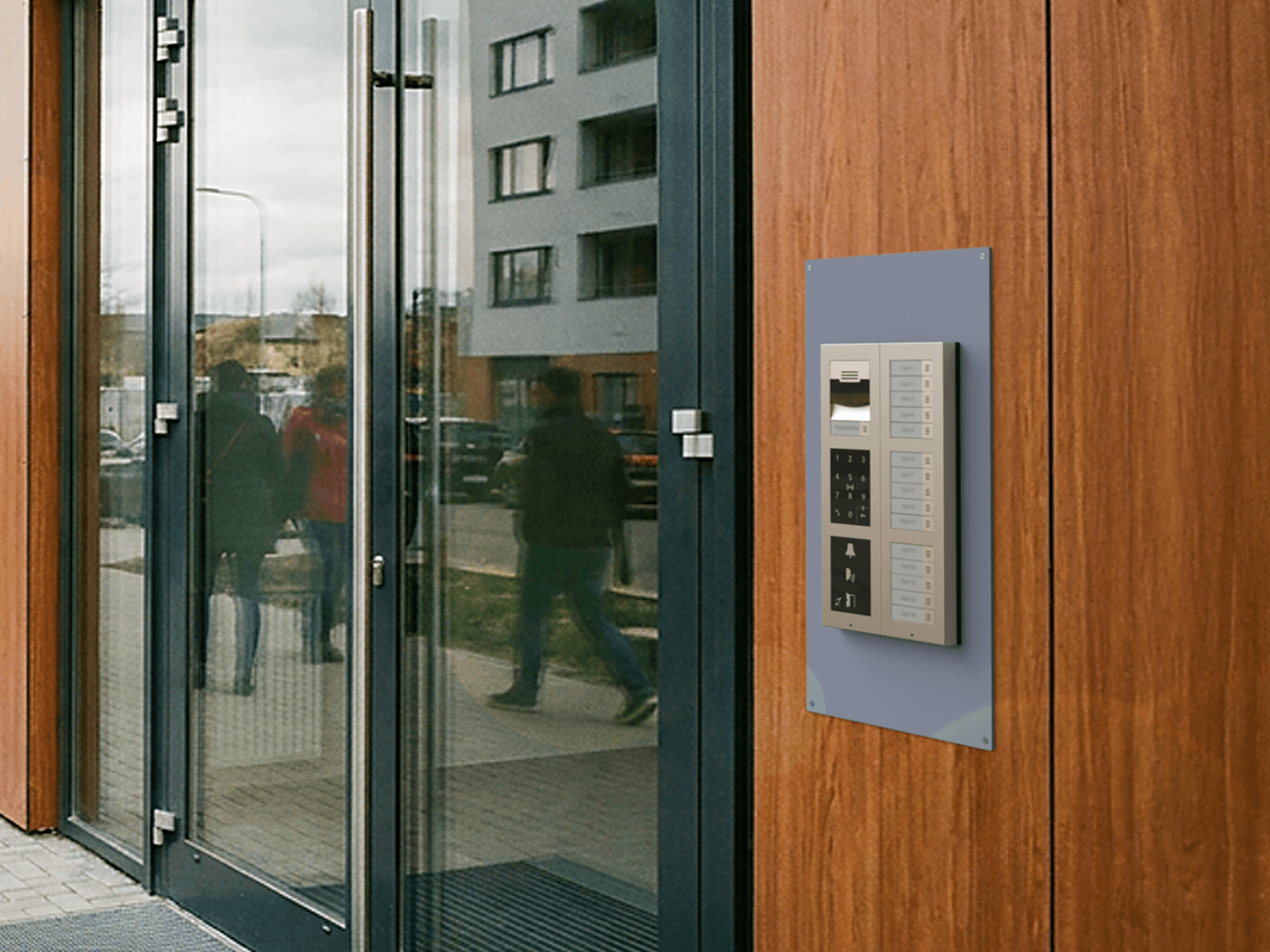 Wall‑mounted intercom panel next to a glass entrance door in a modern residential building exterior.