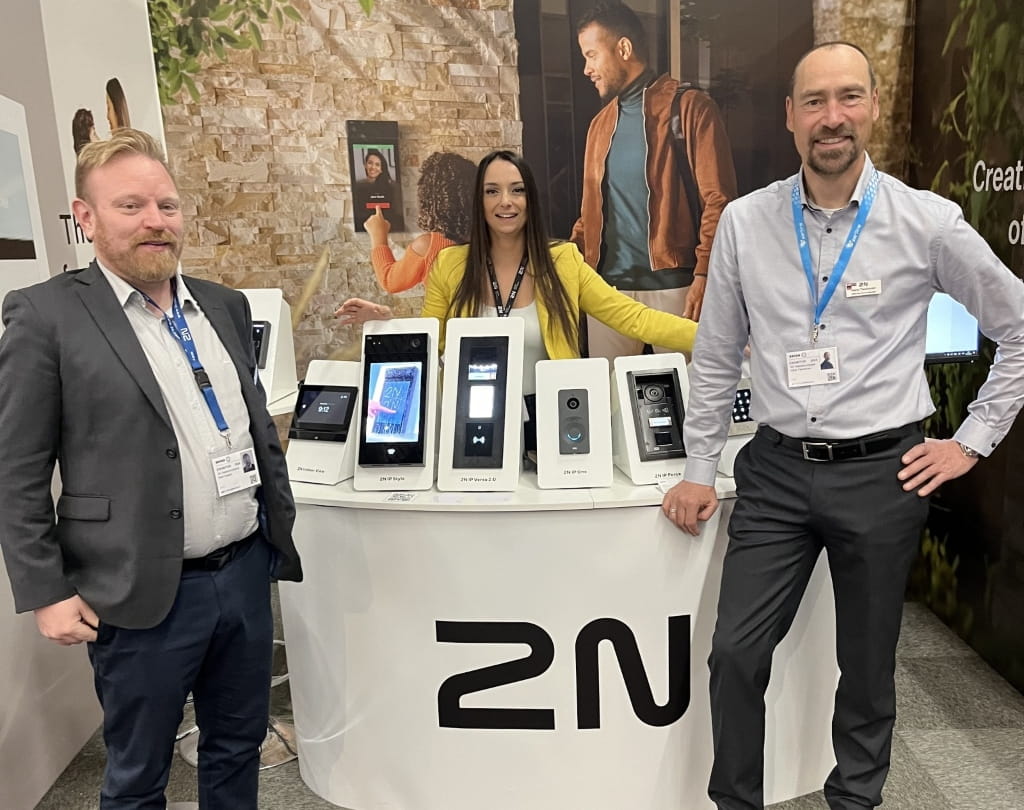 Three individuals standing at a 2N booth displaying multiple access control devices on a white counter.