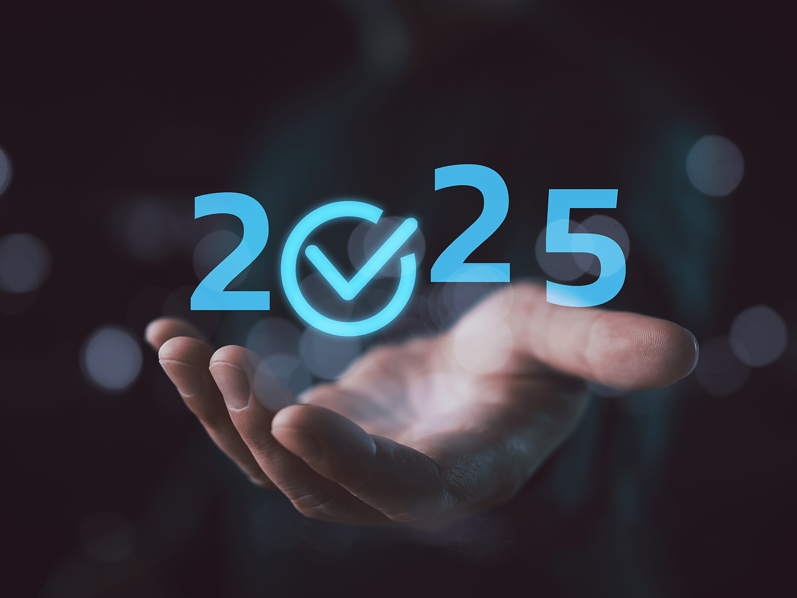  Une main tenant les chiffres bleus lumineux « 2025 » avec une coche à l'intérieur du zéro, qui symbolisent les objectifs futurs.
