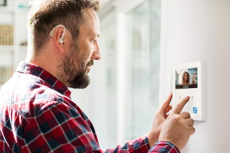 Person interacting with a wall-mounted video intercom screen showing a live image of another individual.