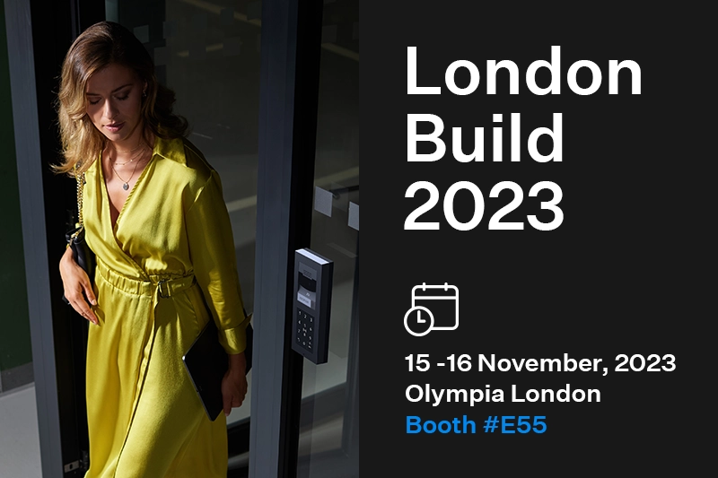 Vrouw in een gele jurk die een gebouw binnenkomt naast de evenementdetails voor London Build 2023.