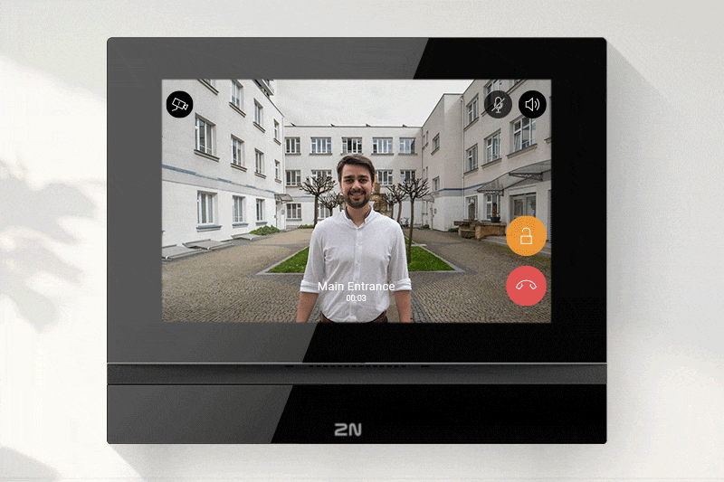 Video call screen on a 2N indoor monitor showing a visitor standing in a residential courtyard.