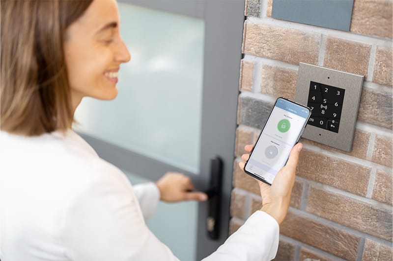 Personne déverrouillant une porte avec un smartphone à côté d'un clavier mural.