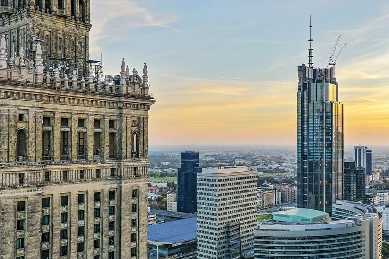 Cityscape with historic and modern high‑rise buildings at sunset, overlooking an urban skyline.
