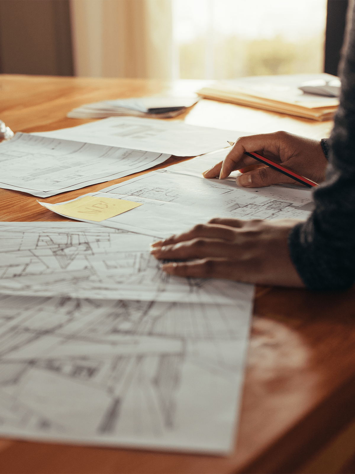 Personne examinant des plans architecturaux et des croquis sur un bureau en bois avec des plans enroulés à proximité