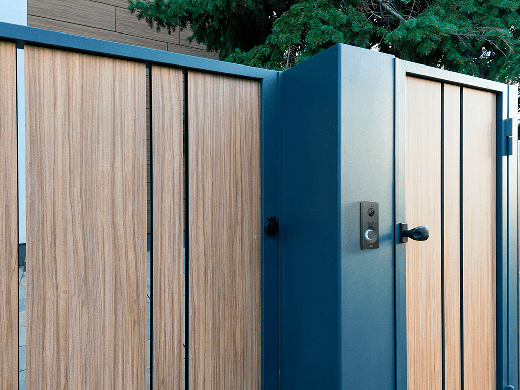 Porta moderna in legno con campanello intelligente integrato e telaio in metallo vicino al verde.