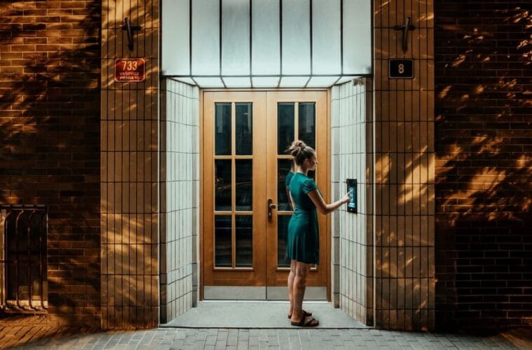 Woman standing at a building entrance at night using a 2N intercom to gain access.