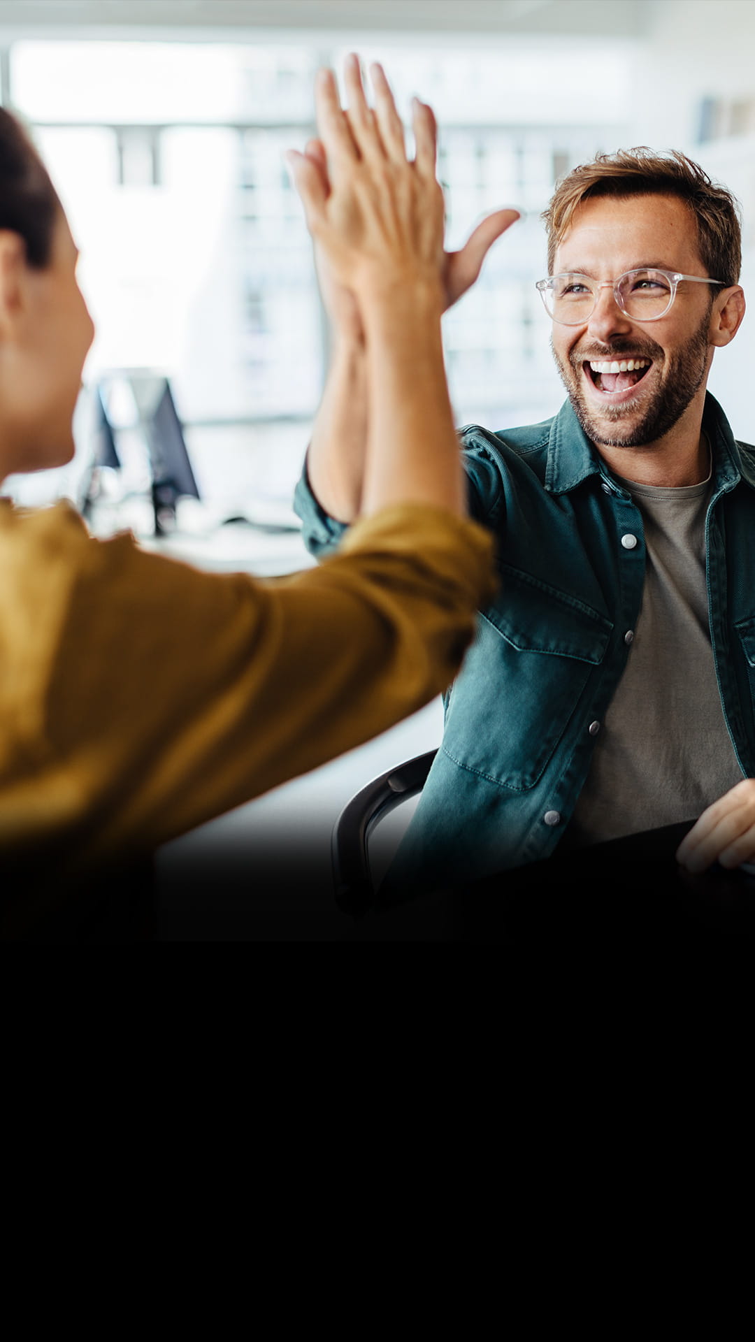 Zwei Personen, die sich in einem Büro mit hellem Tageslicht ein High-Five geben.
