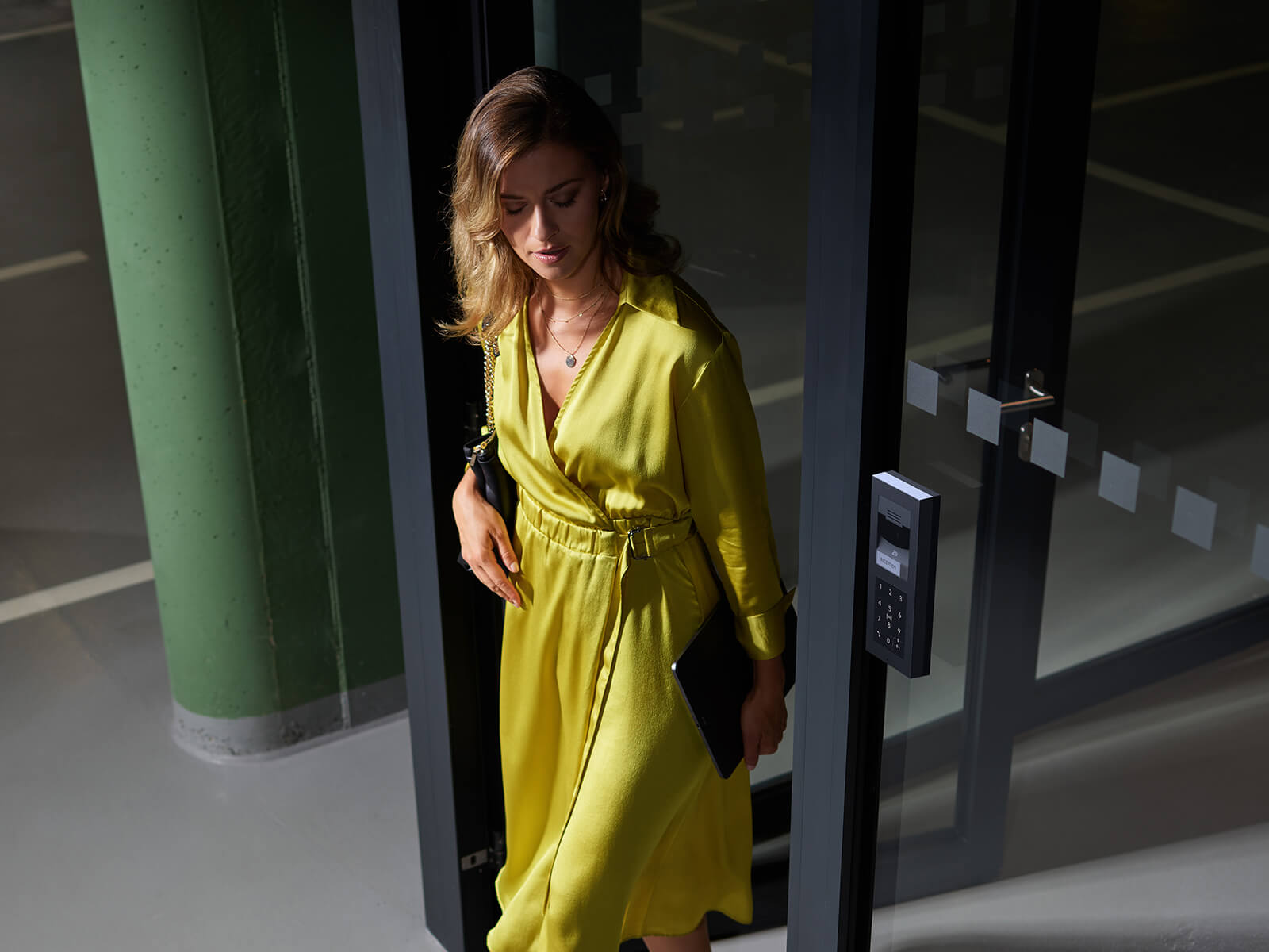 Une personne en tenue jaune vif qui entre par une porte vitrée avec un panneau d'accès électronique.