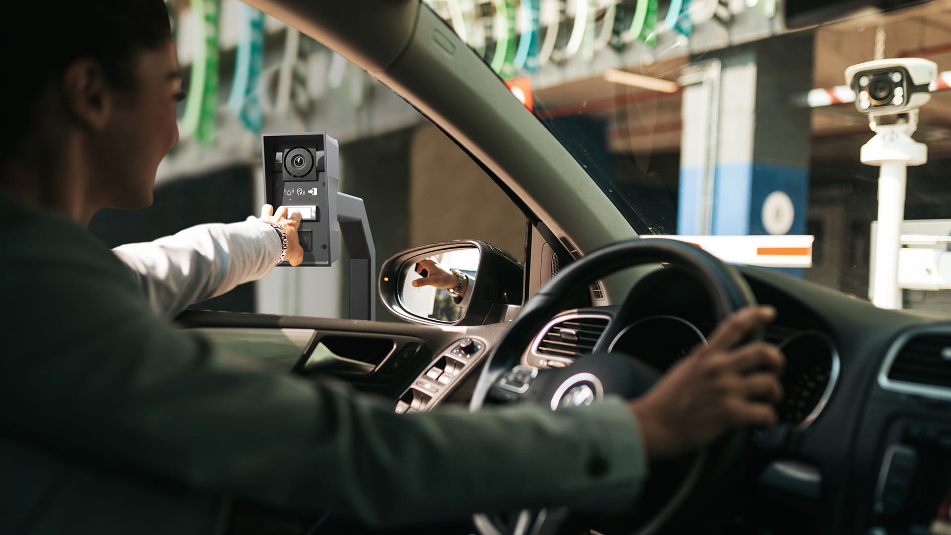 Autista all'interno di un'auto che si avvicina a un dispositivo di controllo accessi all'ingresso di un parcheggio.