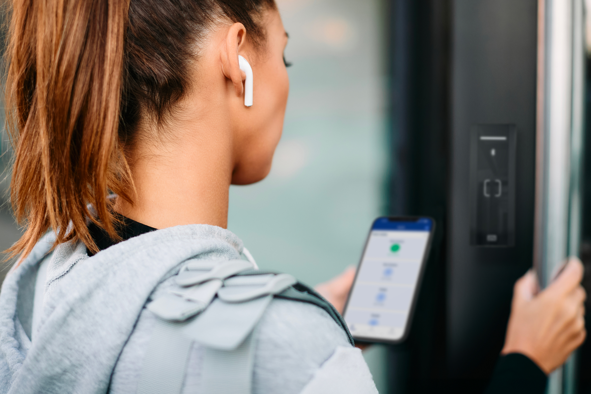 Persoon met een smartphone met een toegang-app bij een zwarte RFID-lezer op een glazen deur.