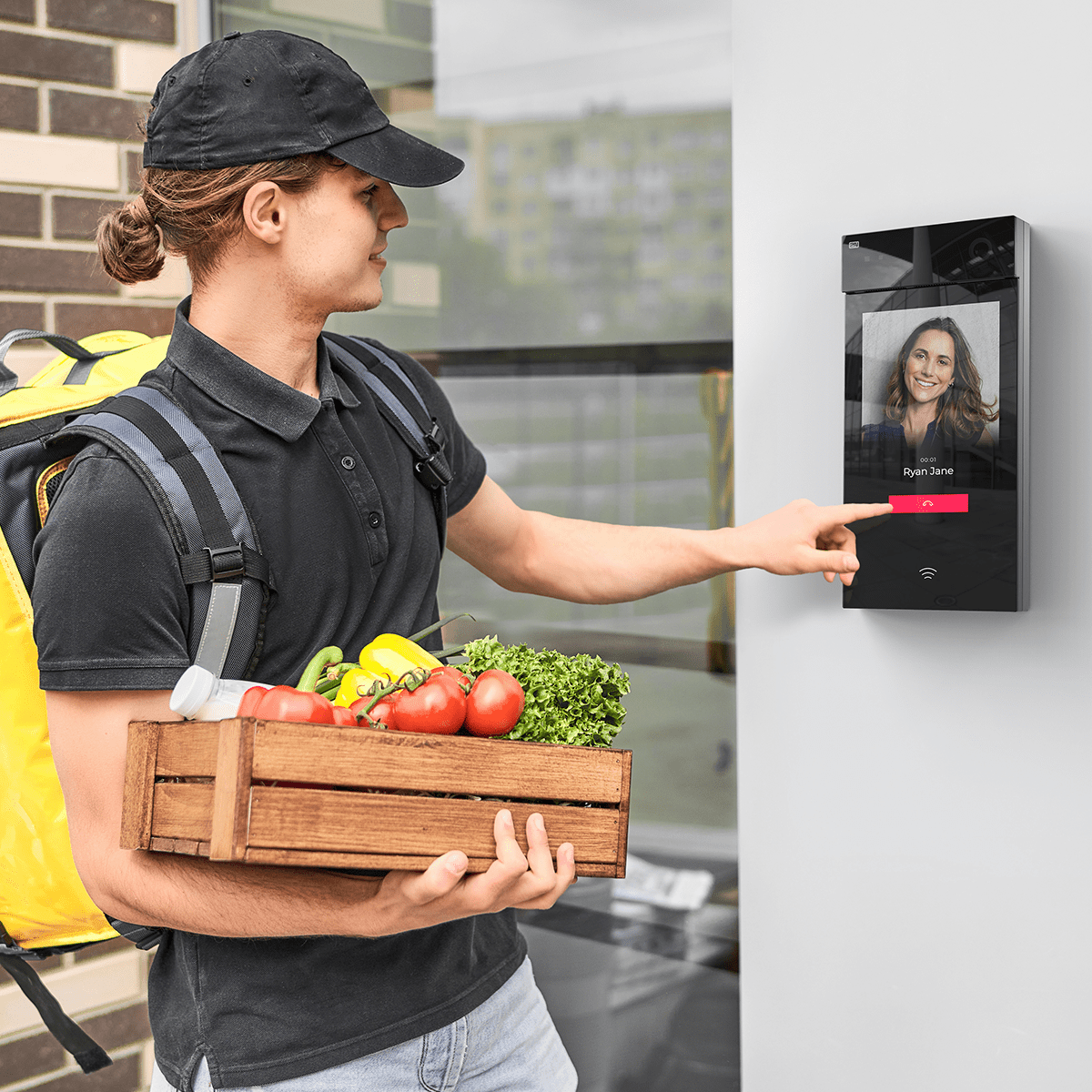Koerier met boodschappen die een 2N-touchscreenintercom gebruikt om een bewoner bij de ingang van een appartement te bellen.