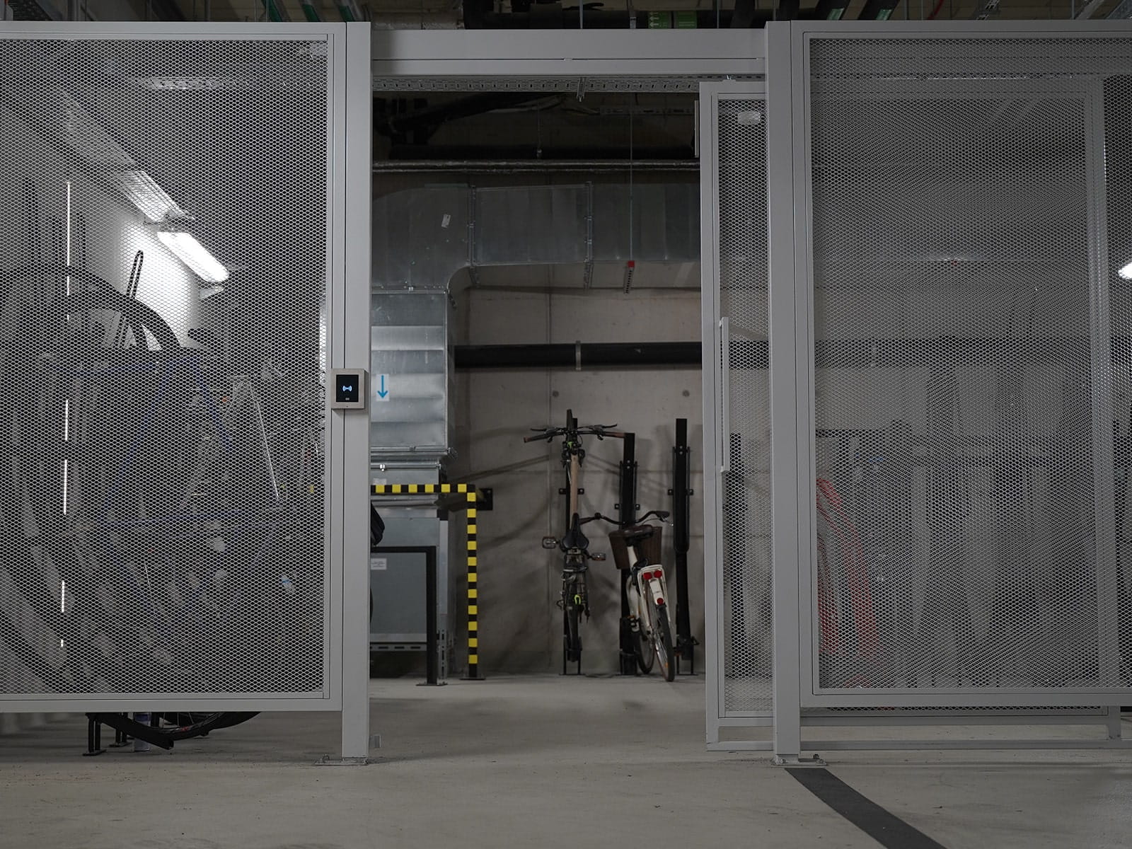 Área segura para guardar bicicletas dentro de casa, com portas de malha metálica e um painel de controlo de acesso eletrónico.