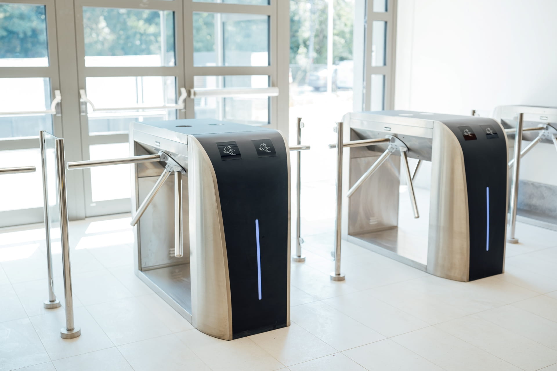 Deux tourniquets modernes avec des bras en métal dans une zone d'entrée intérieure lumineuse.