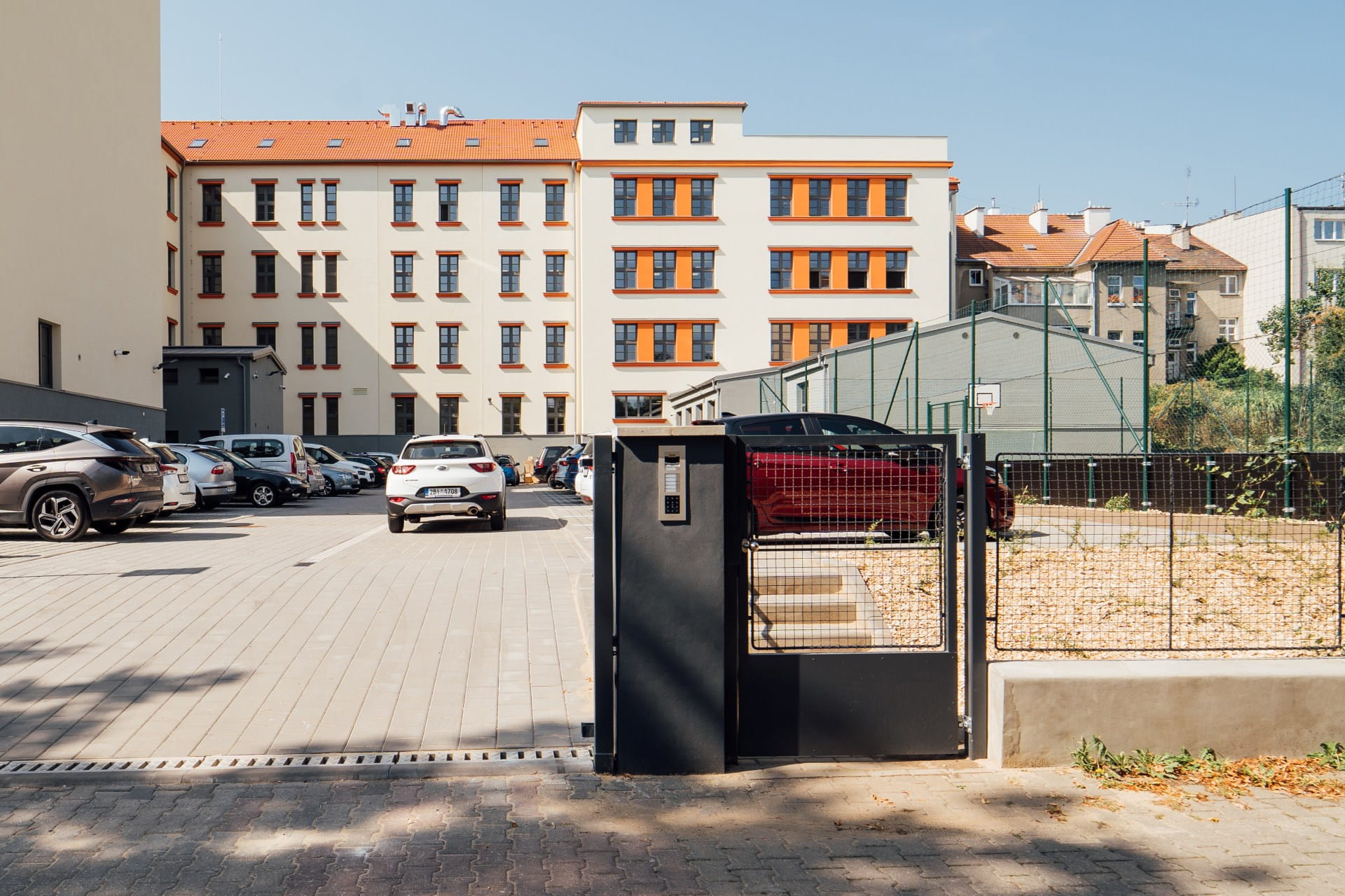 Portail sécurisé avec interphone et clavier à l'entrée d'un parking près d'un bâtiment moderne.