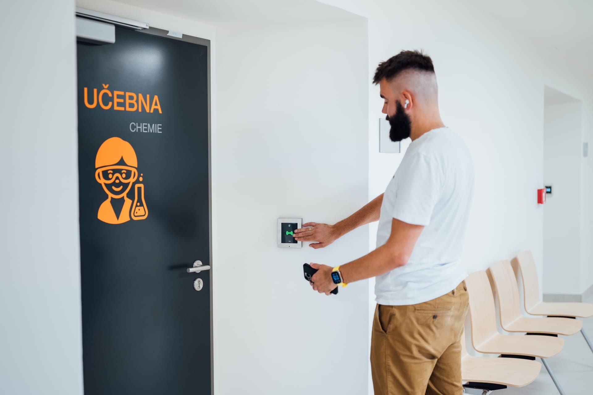 Personne utilisant un lecteur de carte pour le contrôle d'accès à côté d'une porte de salle de classe étiquetée "UČEBNA CHEMIE."