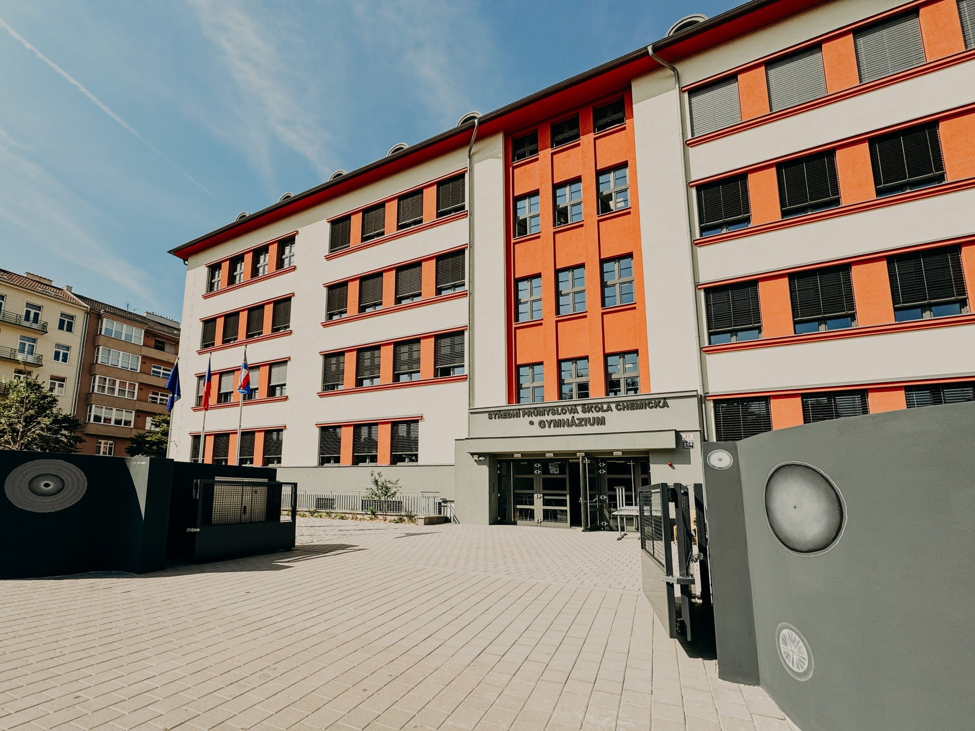 École moderne avec une façade orange et grise, entrée principale visible derrière une cour fermée.