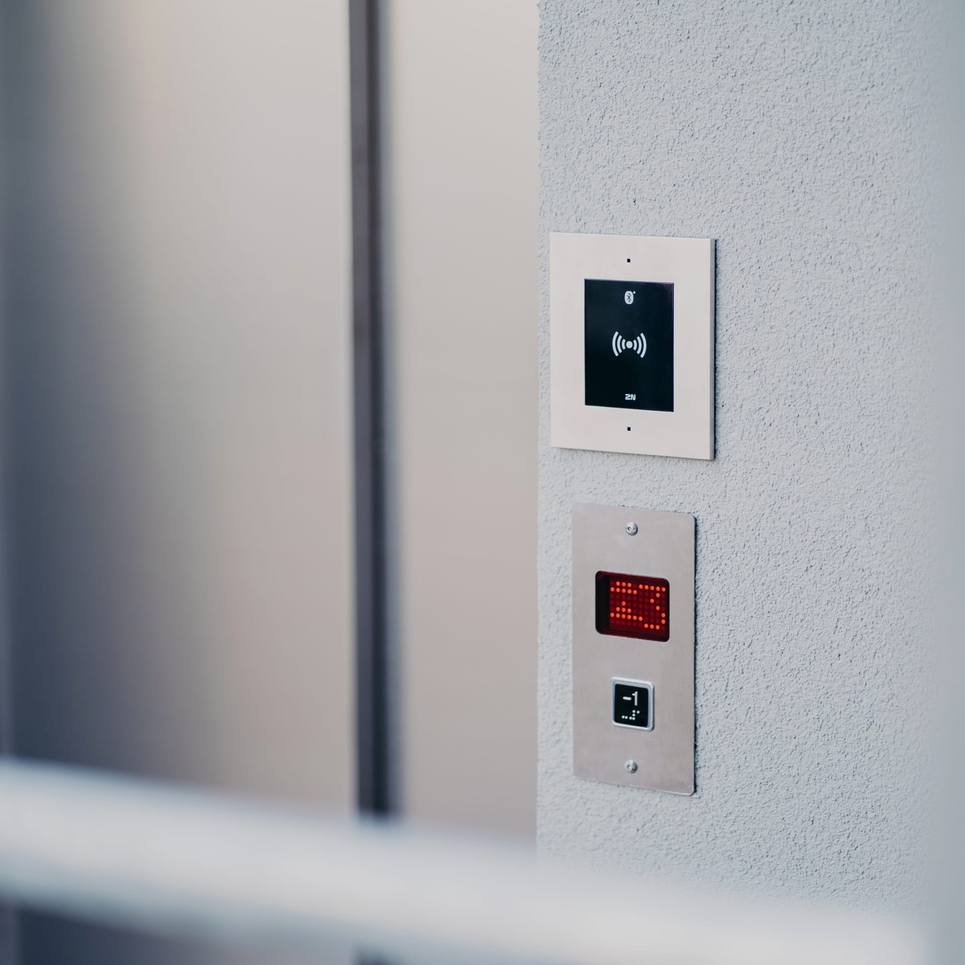 Panneau de contrôle d'ascenseur avec un lecteur de carte et un bouton d'appel lumineux sur un mur de couleur claire.