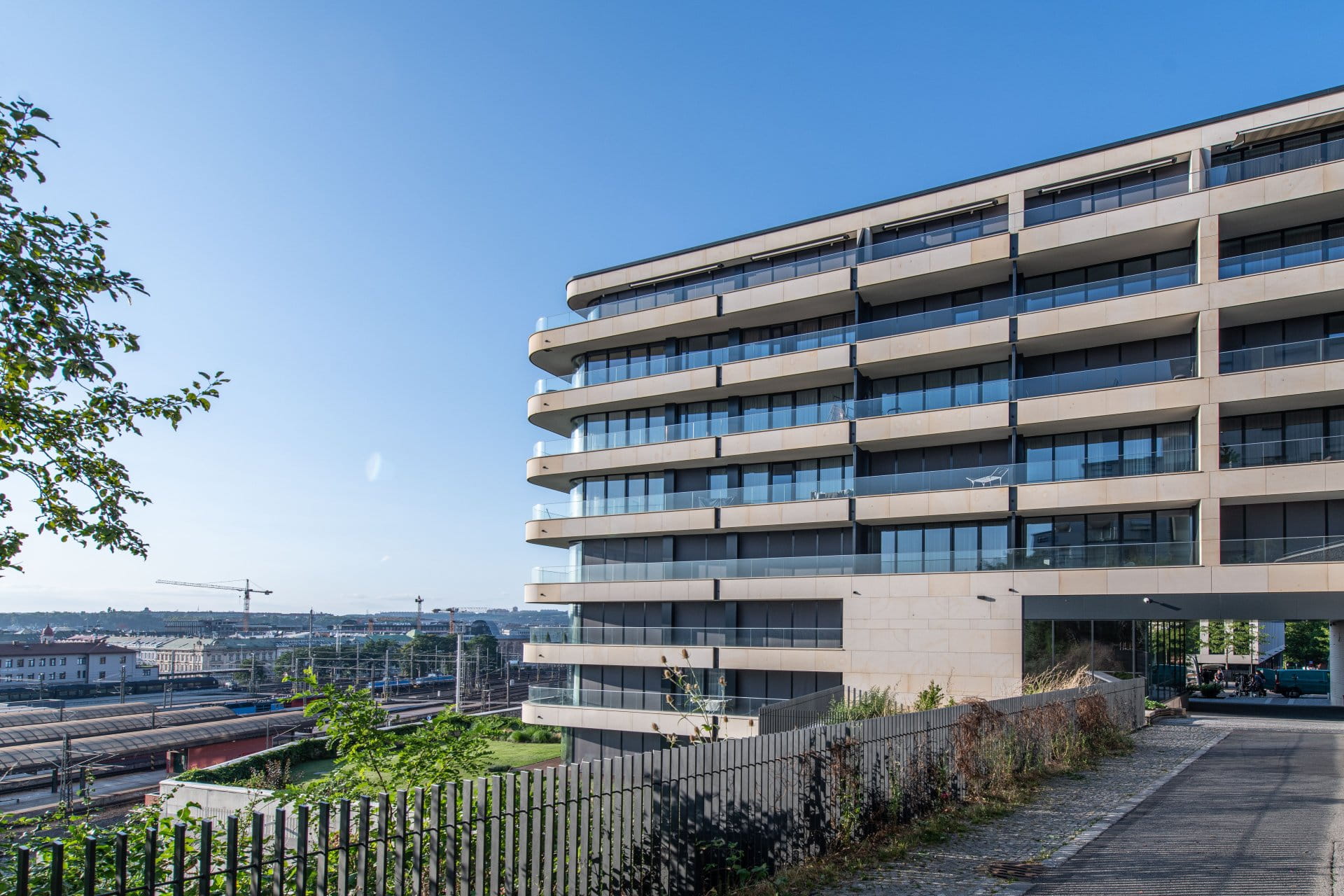 Immeuble moderne de plusieurs étages avec de grands balcons vitrés donnant sur la ville et les voies ferrées.