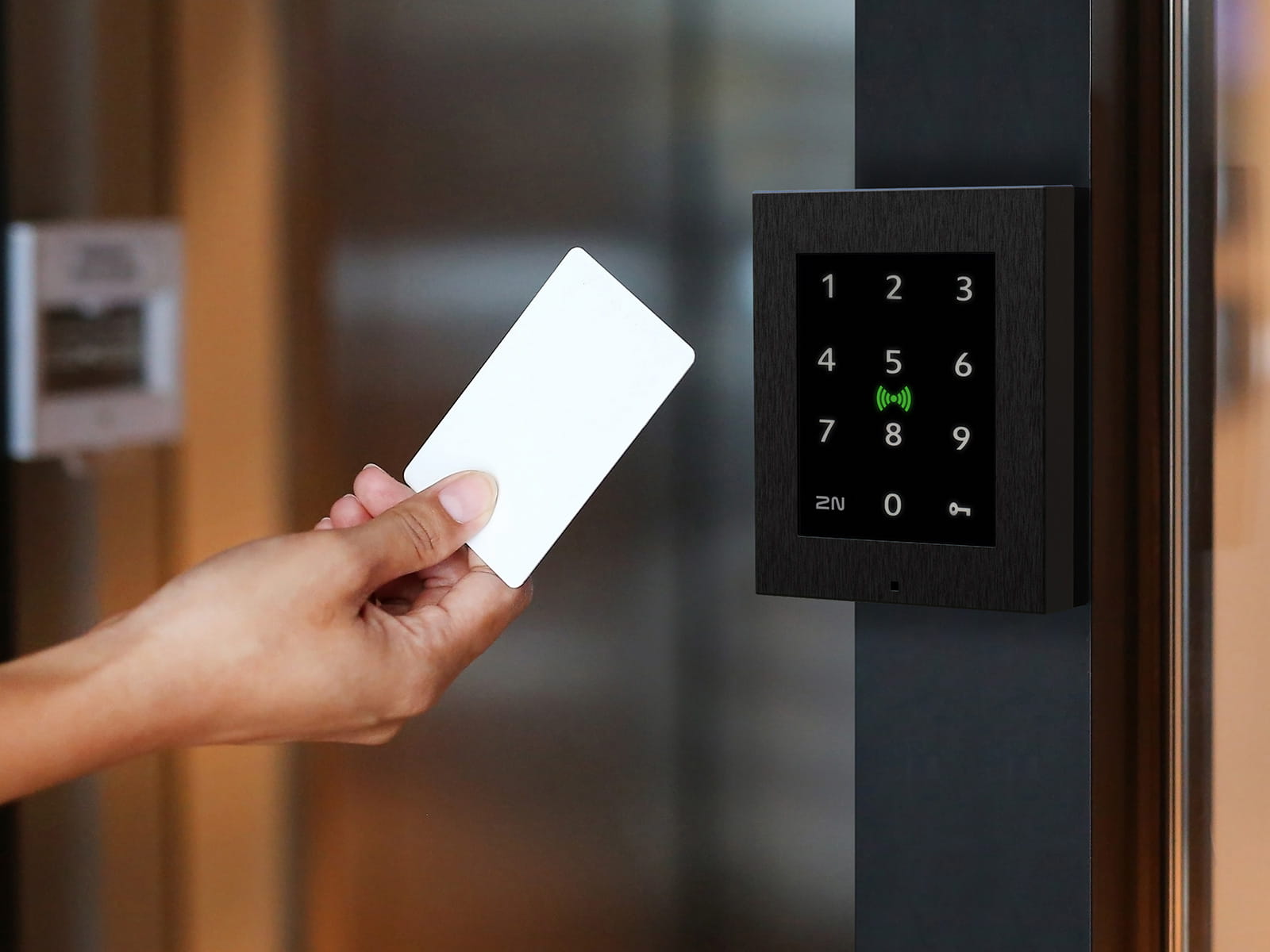 Main tenant une carte d'accès blanche près d'un lecteur de clavier noir monté sur un mur pour une entrée sécurisée.
