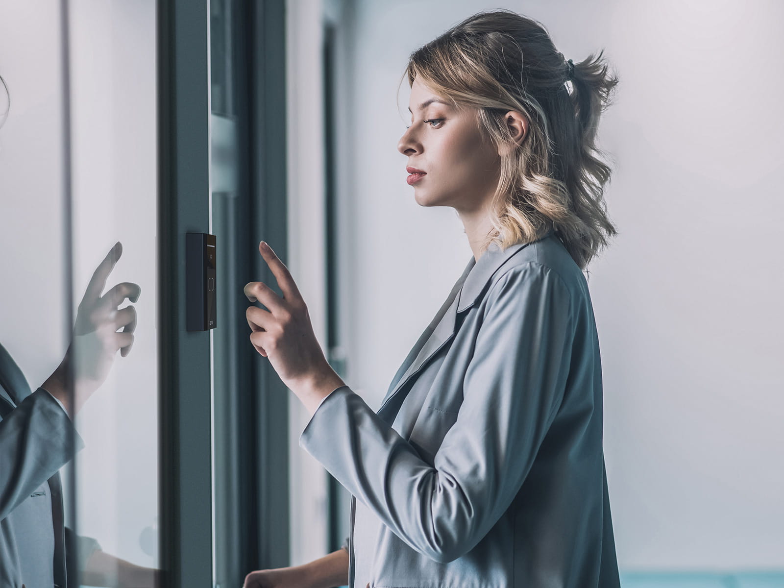 Person standing near a glass door, reaching toward an access control reader mounted on the frame.
