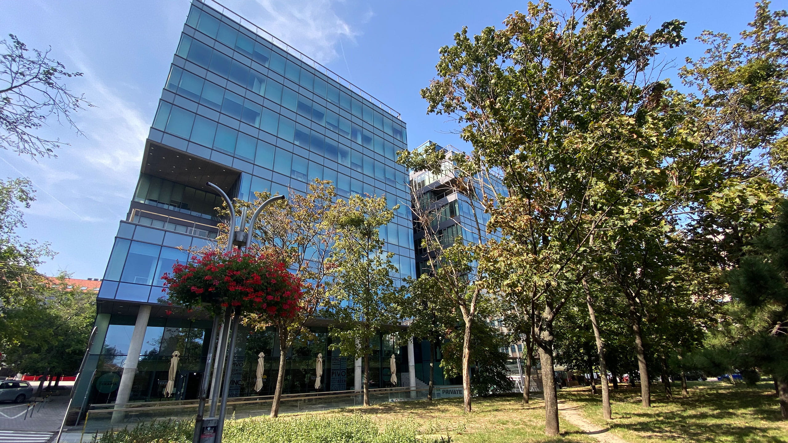 Modern glass office building surrounded by trees and greenery on a sunny day.