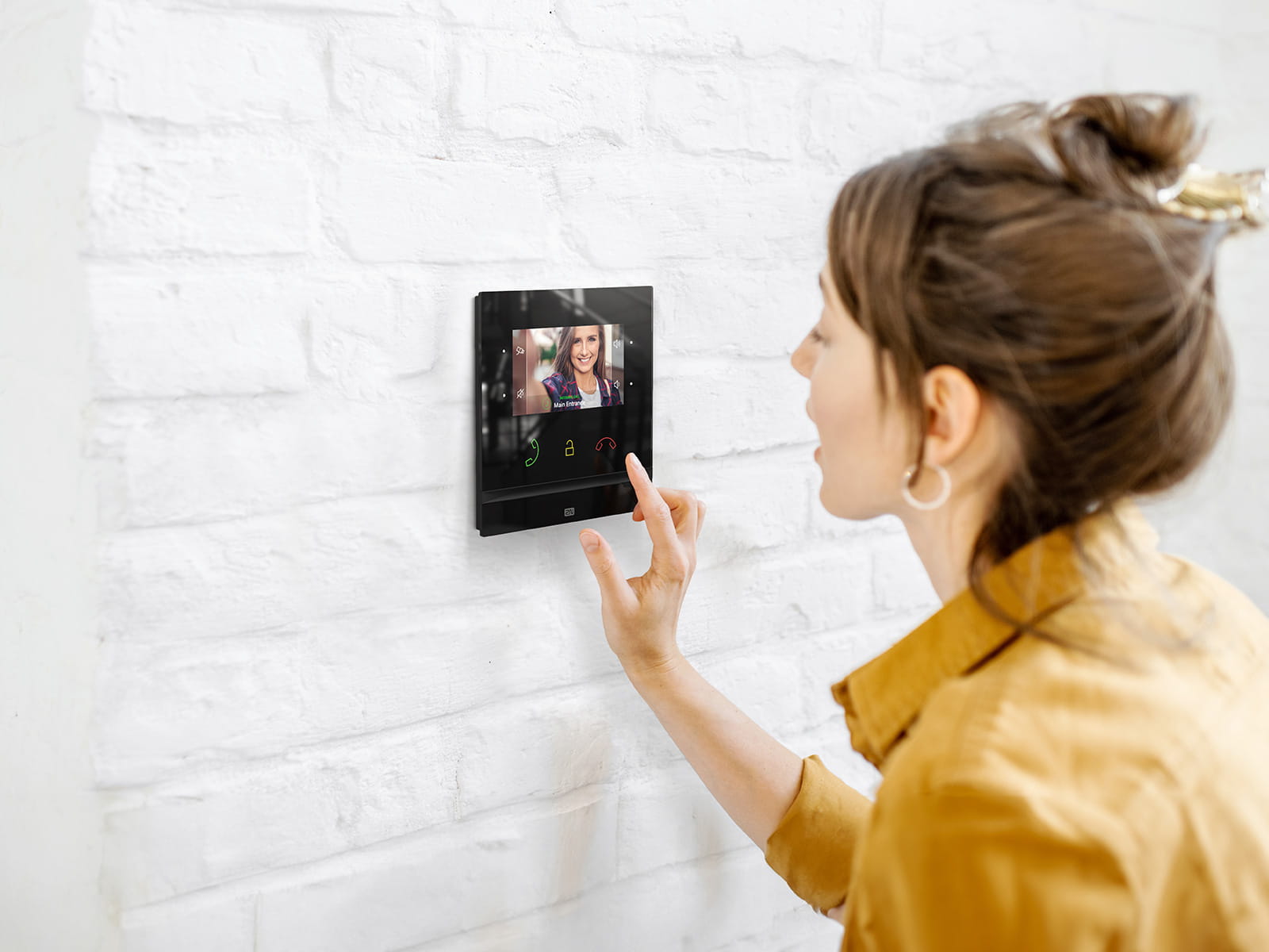 Personne utilisant un interphone vidéo à écran tactile monté sur le mur affichant deux visiteurs à l'écran.