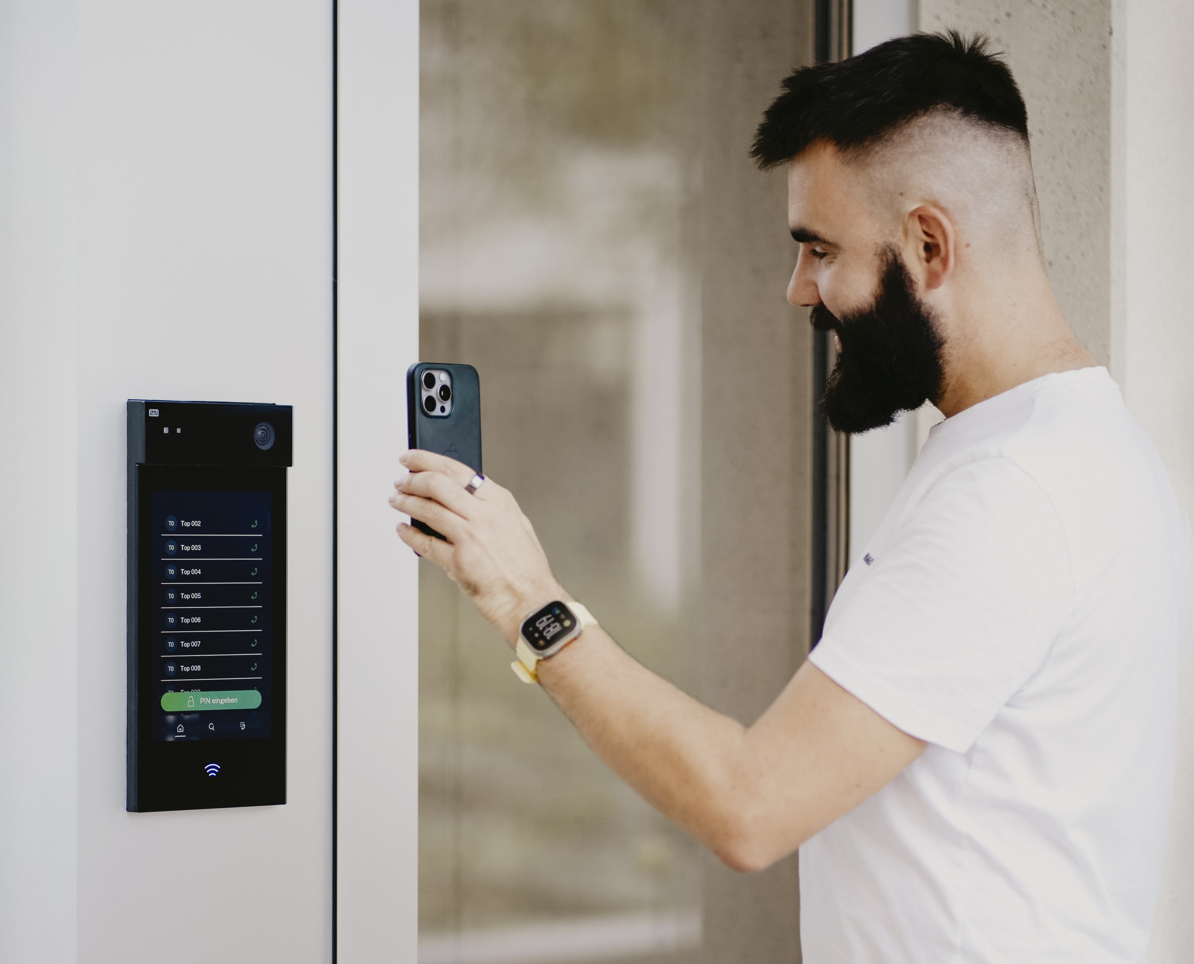 Quelqu'un qui utilise son smartphone pour ouvrir une porte grâce à un panneau de contrôle accroché au mur.