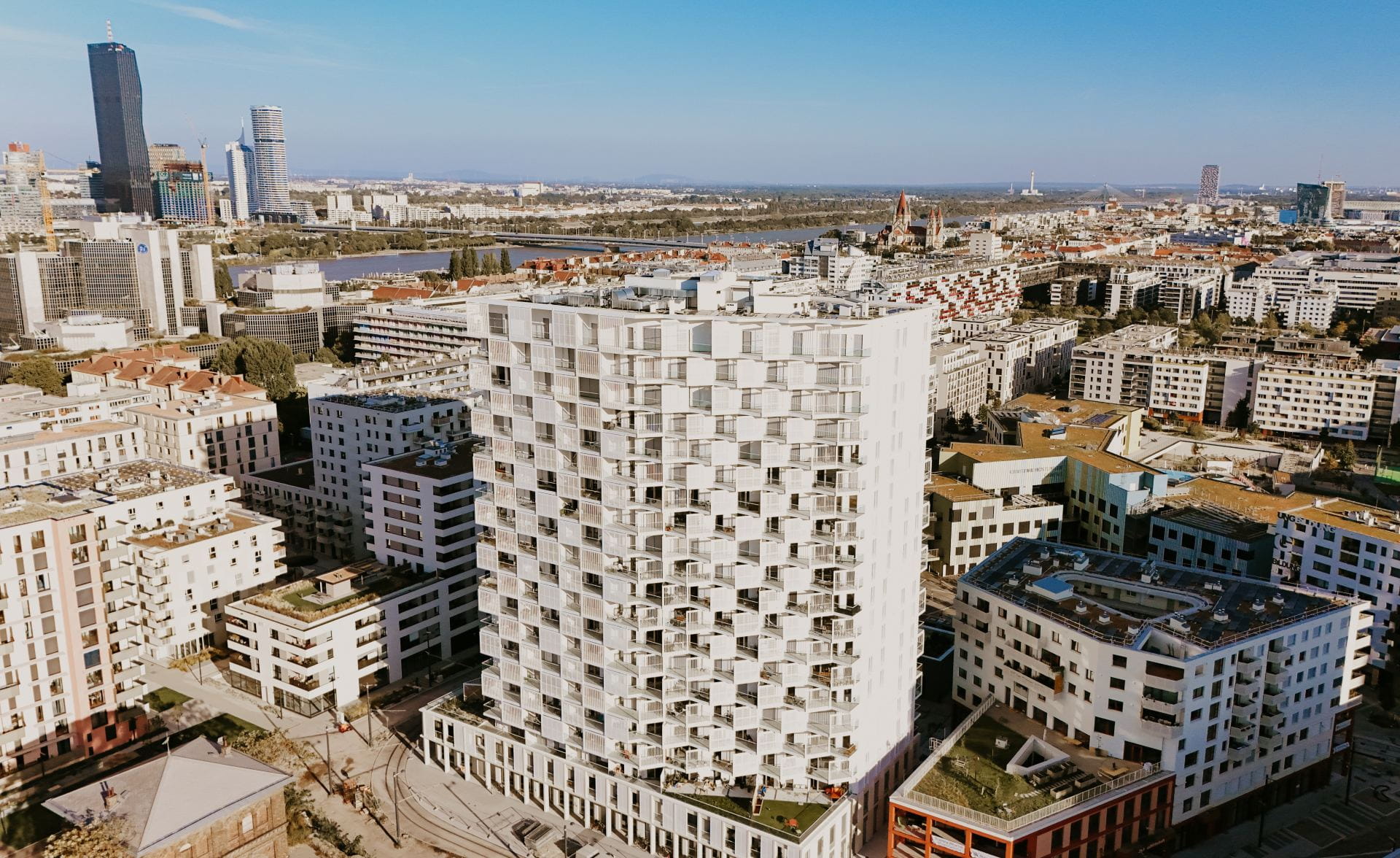 Vue aérienne d'un bâtiment moderne blanc en hauteur avec une façade géométrique entouré d'un paysage urbain.