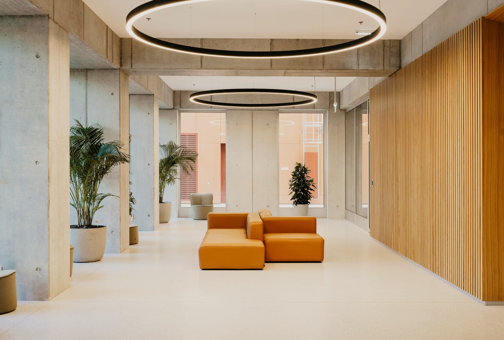 Hall d'entrée spacieux et moderne avec des sièges modulaires orange, de grands plafonniers ronds et des plantes en pot.