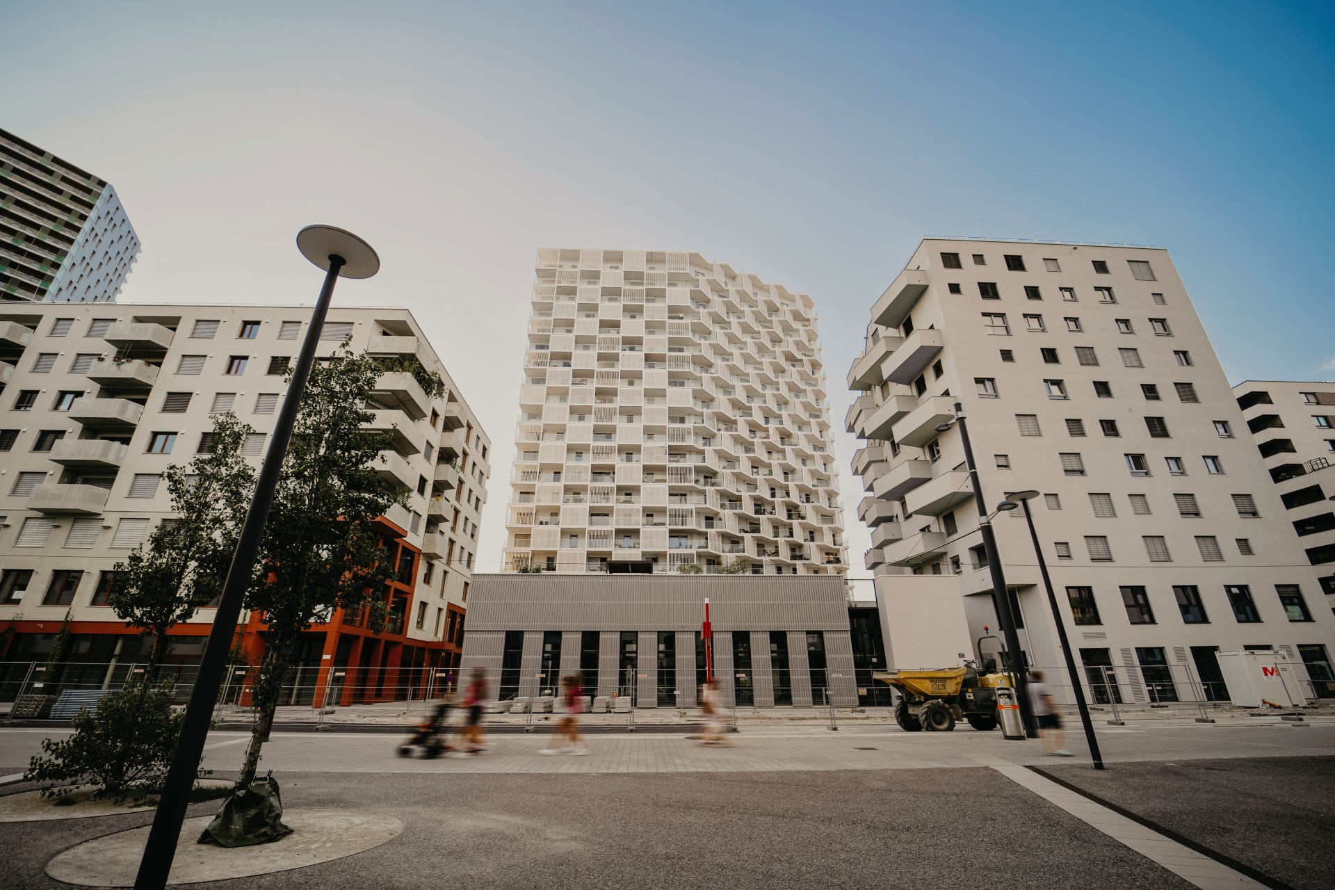 Des immeubles modernes avec des façades géométriques dans une place urbaine sous un ciel dégagé.