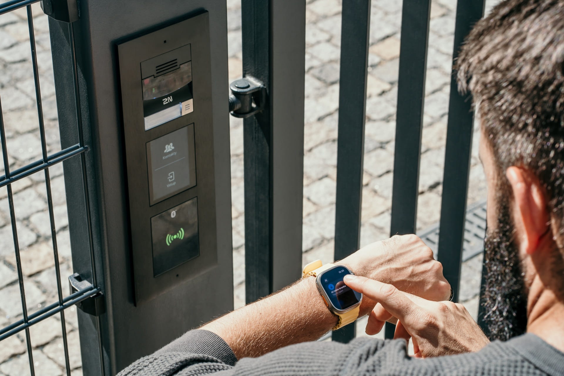 Personne utilisant une montre intelligente pour accéder à un portail avec un système d'interphone électronique.