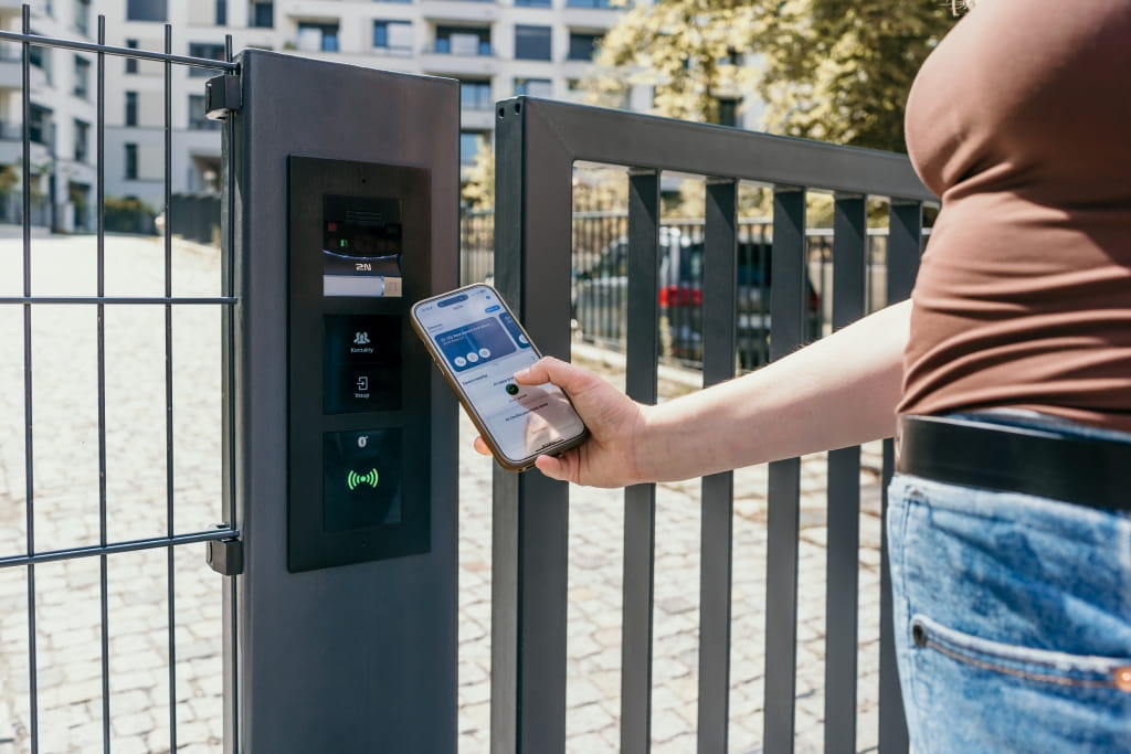 Quelqu'un qui tient un smartphone près d'un interphone de portail pour s'identifier sur son téléphone.