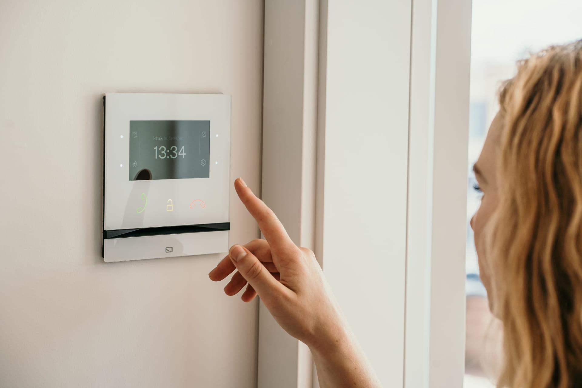 Personne interagissant avec un appareil intercom à écran tactile monté sur le mur à l'intérieur.