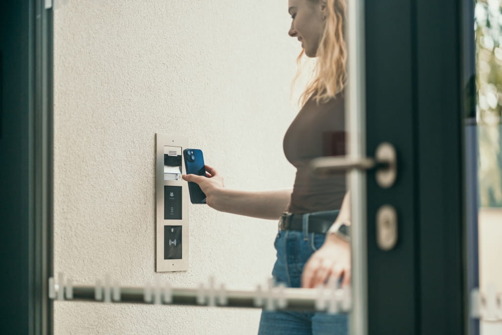 Personne utilisant un smartphone pour un accès sans contact à un panneau d'interphone extérieur.