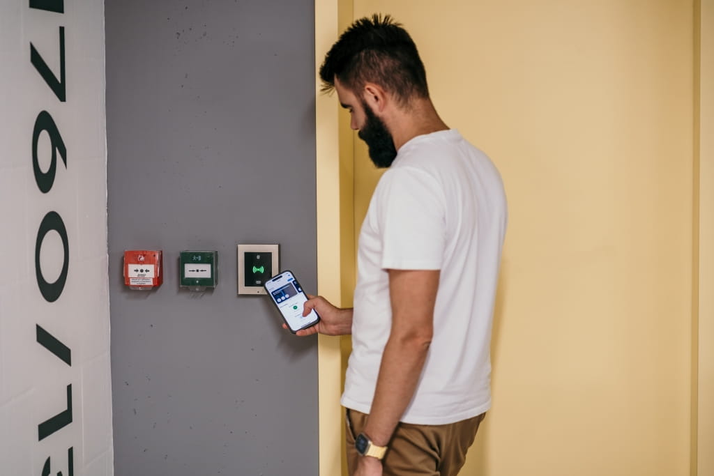 Personne utilisant un smartphone pour déverrouiller une porte via un lecteur de contrôle d'accès monté sur le mur.