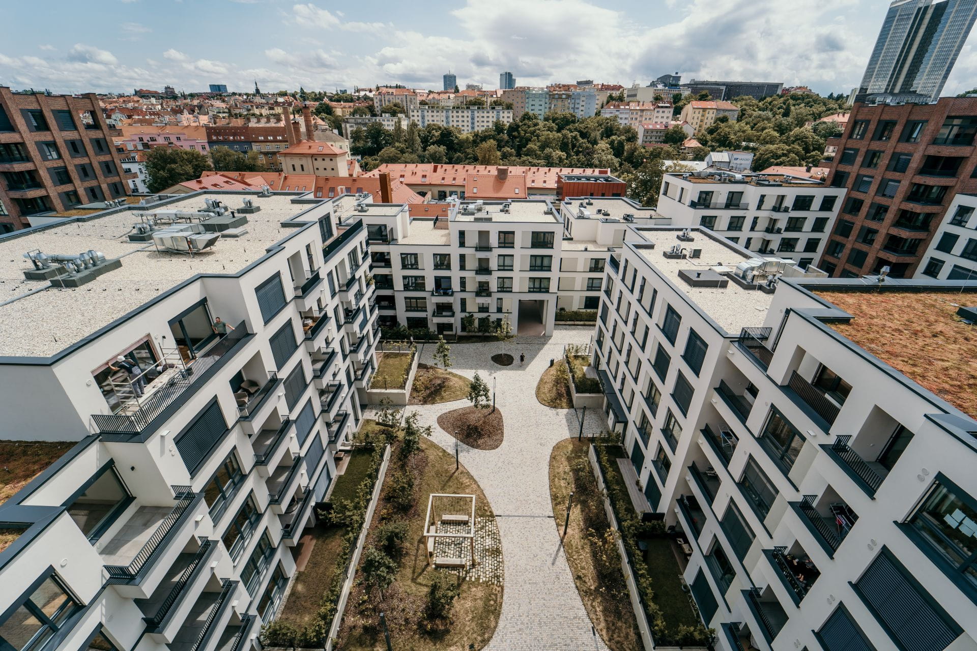 Vue aérienne d'immeubles d'appartements modernes avec une cour paysagée et la silhouette de la ville en arrière-plan.